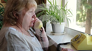 Serious elderly woman speaking on phone. Grandmother talking on old disc phone