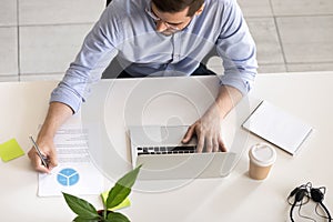 Serious employee using laptop, making notes, top view