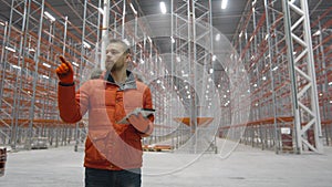 Serious engineer checks documents on tablet inside new modern warehouse