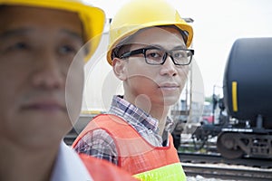 Serious engineer in protective workwear looking at camera outside in front of railroad tracks