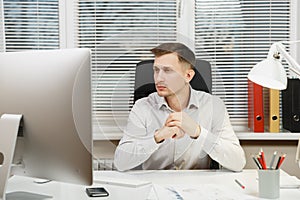 Serious and engrossed business man in shirt sitting at the desk, working at computer with modern monitor. Manager or worker.