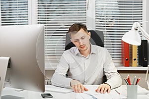 Serious and engrossed business man in shirt sitting at the desk, working at computer with modern monitor. Manager or worker.