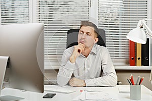 Serious and engrossed business man in shirt sitting at the desk, working at computer with modern monitor. Manager or worker.