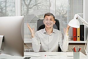 Serious and engrossed business man in shirt sitting at the desk, working at computer with modern monitor. Manager or worker.