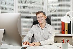 Serious and engrossed business man in shirt sitting at the desk, working at computer with modern monitor. Manager or worker.