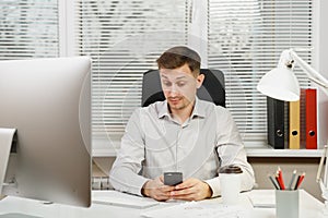 Serious and engrossed business man in shirt sitting at the desk, working at computer with modern monitor. Manager or worker.