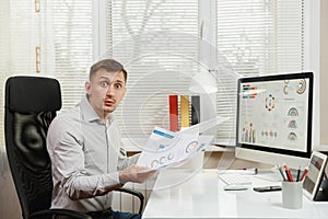 Serious and engrossed business man in shirt sitting at the desk, working at computer with modern monitor. Manager or worker.