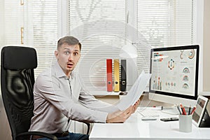 Serious and engrossed business man in shirt sitting at the desk, working at computer with modern monitor. Manager or worker.