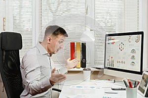 Serious and engrossed business man in shirt sitting at the desk, working at computer with modern monitor. Manager or worker.