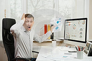 Serious and engrossed business man in shirt sitting at the desk, working at computer with modern monitor. Manager or worker.