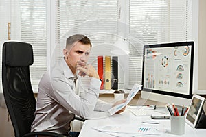 Serious and engrossed business man in shirt sitting at the desk, working at computer with modern monitor. Manager or worker.