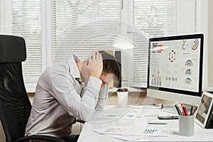 Serious and engrossed business man in shirt sitting at the desk, working at computer with modern monitor. Manager or worker.