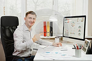 Serious and engrossed business man in shirt sitting at the desk, working at computer with modern monitor. Manager or worker.