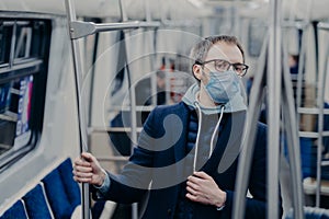 Serious European man being aware of his health, protects from catching serious disease in public transport, wears medical mask on