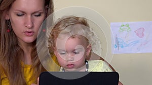 Serious face woman teaching baby girl using tablet computer. Closeup