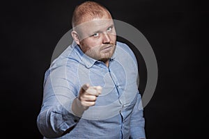 A serious fat redhead man with a beard points a finger. Black background