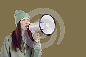 Serious female activist with megaphone in her hand makes loud announcement on brown background.