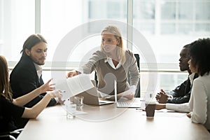 Serious female boss handing paper report to employee at meeting