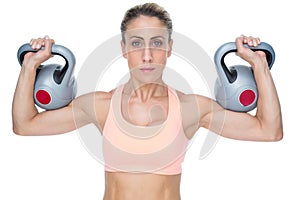 Serious female crossfitter lifting kettlebells looking at camera