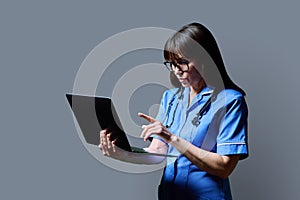 Female nurse using laptop, profile view on gray studio background