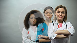 Serious female nurses with red ribbons and hands crossed, AIDS awareness concept