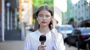 Serious female reporter with microphone in front of camera, breaking news photo