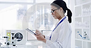 Serious female scientist working and writing patient information in a lab. Laboratory worker looking at and analyzing