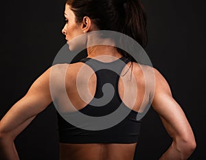 Serious female sporty muscular with ponytail doing stretching workout the shoulders, blades and arms in sport bra, standing on