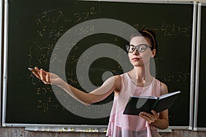 serious female teacher explain math formulas in university beside blackboard