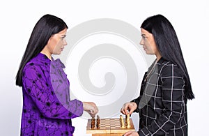 Serious female twins play chess and look eye to eye on a white background. Chess game concept