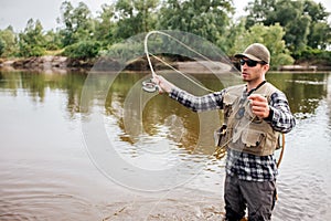 Serious fisherman stands on shallow an waving with fly-fishing. Also he has a spoon in other hand. Guy is looking to the