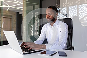 Serious focused african american programmer working inside office, man coding new software on laptop, mature experienced