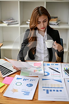 A serious and focused Asian businesswoman analyzing business financial reports at her desk