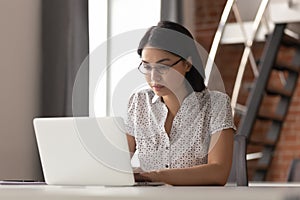 Serious focused asian female employee in glasses working with computer.