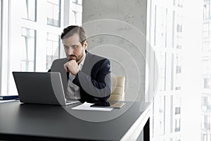 Serious focused businessman using laptop working seated at modern office