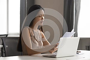 Serious focused busy young female asian employee reading financial report.
