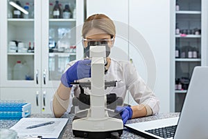 Serious and focused female researcher working with microscope inside laboratory, mature and experienced scientist