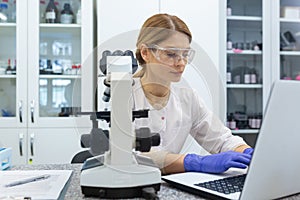 Serious and focused female researcher working with microscope inside laboratory, mature and experienced scientist