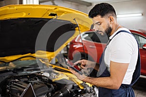 Serious focused man car technician mechanic repairing car problem of engine, during system checking