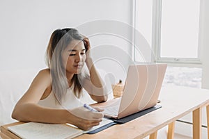 Serious freelance woman is working online at home with computer laptop and taking notes in her apartment.