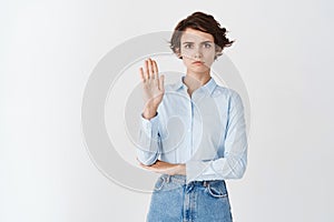 Serious frowning woman say no, showing stop gesture, forbid action or condemn something, standing on white background