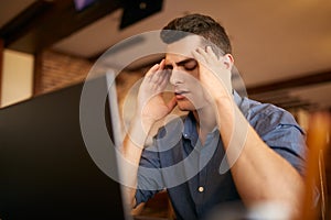 Serious frustrated businessman with closed eyes suffering from headache migraine at workplace, massaging temples