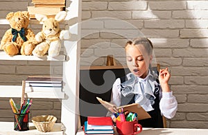 Serious funny school girl reading book in classroom at school. Kid studying at school. Schoolchild doing homework at