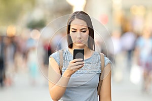 Serious girl checking phone message on the street