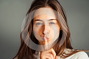 Serious girl holding a finger near her mouth, on a gray background. no makeup, no retouching