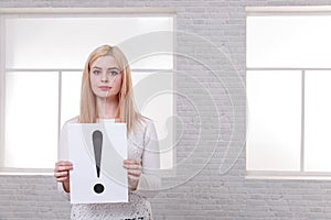 Serious girl, holds a white sheet with a blck exclamation point.