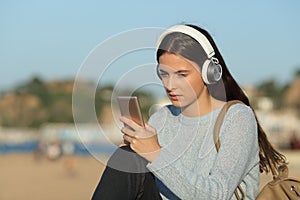 Serious girl listening to music checking smart phone