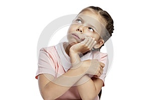 A serious girl with pigtails sits at a table. Isolated over white background