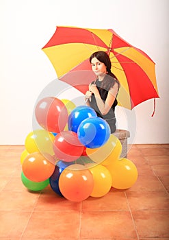 Serious girl with red and yellow umbrella behind inflating balloons