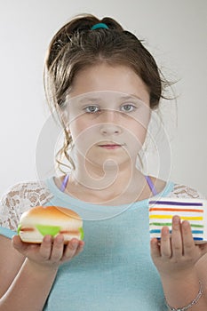 A serious girl with a sguishy toy cake and burger in her hands